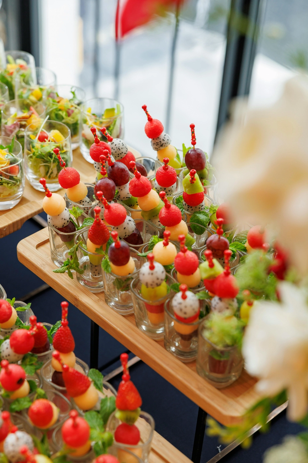 Brunchy. - Restaurant - Zahlreiche Portionen Obstspieße, serviert in kleinen Gläsern auf Holztabletts, vermutlich für ein Catering oder eine Party.